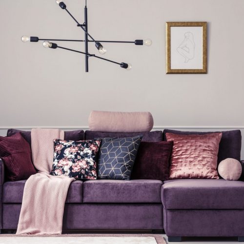 Modern lamp and violet sofa decorated with patterned pillows in a living room interior