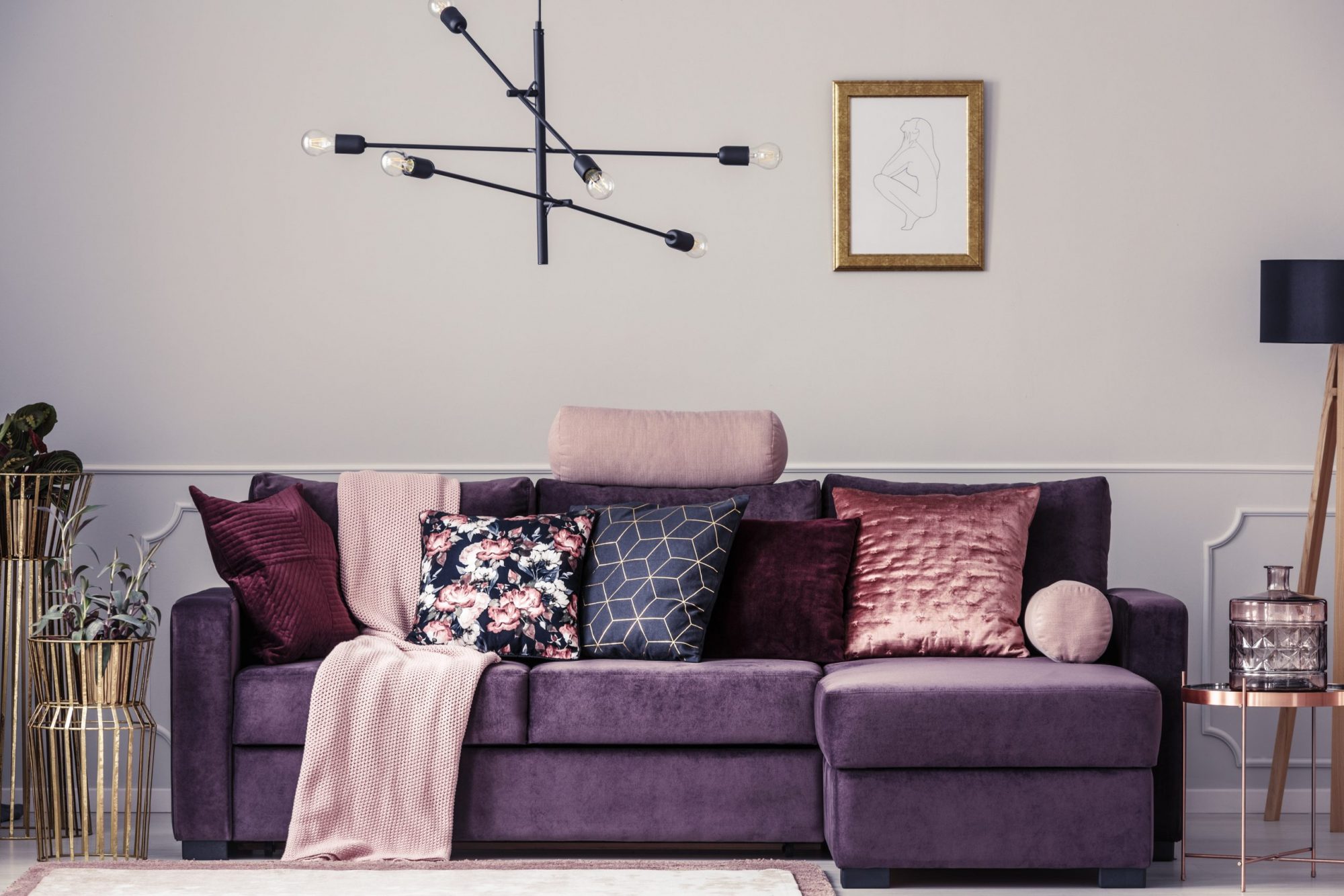 Modern lamp and violet sofa decorated with patterned pillows in a living room interior